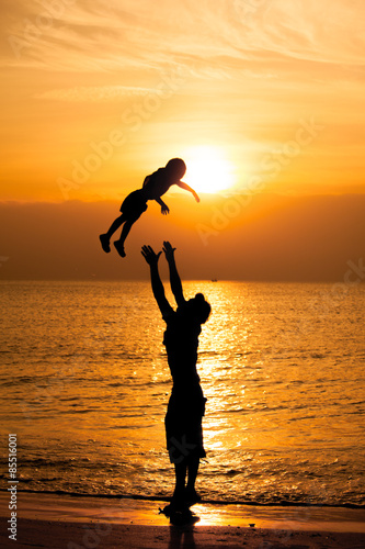 Silhouette of father carrying child on the beach during sunset.