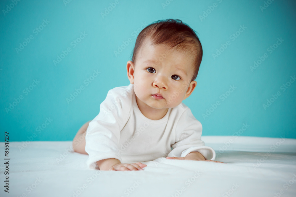 Cute Asian baby girl lying on stomach on bed, studio shot Cute Asian baby girl lying on stomach on bed, studio shot