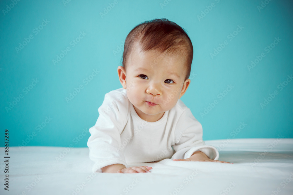 Cute Asian baby girl lying on stomach on bed, studio shot Cute Asian baby girl lying on stomach on bed, studio shot