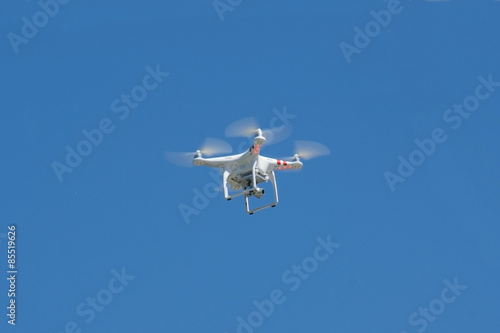 white drone hovering in a bright blue sky