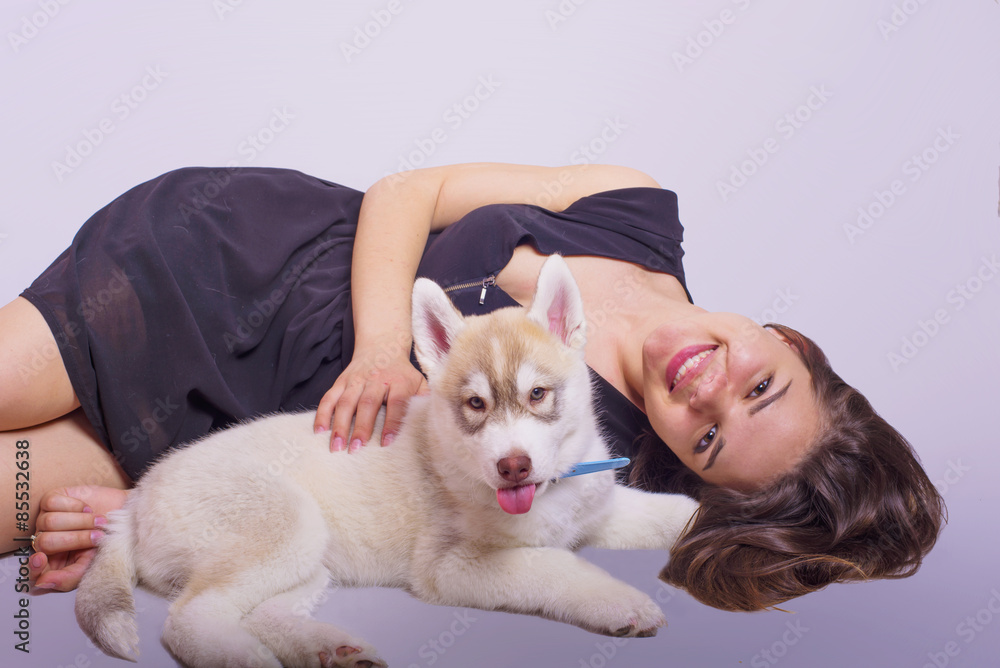 young caucasian female playing with a puppy, girl and siberian husky studio shot on grey background young caucasian female playing with a puppy, girl and siberian husky studio shot on grey background