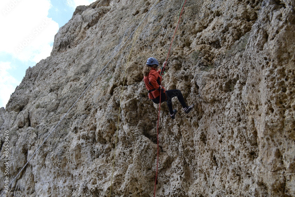 Ragazza alle prese di una discesa da una roccia Ragazza alle prese di una discesa da una roccia