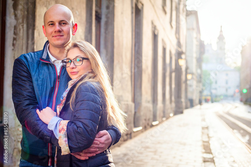 Young fashion elegant stylish couple, travel by old European cities, posing hugging each other, smiling, girl in glasses