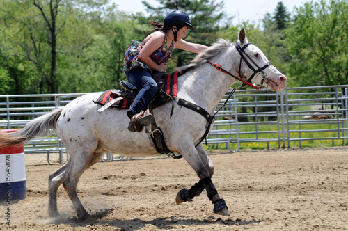 Teenage girl galloping past a barrel during a barrel race