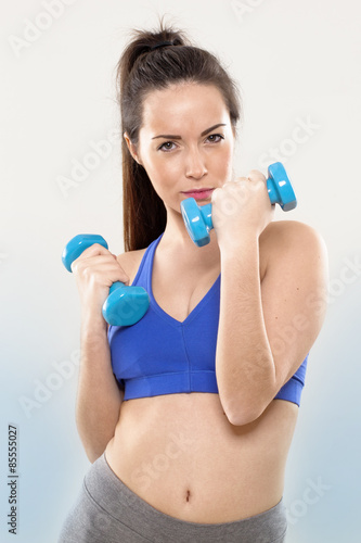 proud athletic woman wearing blue gym bra showing muscle power and toning with dumbbell holding