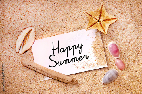 Happy summer written on a note on white beach sand, starfish and shells