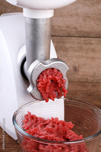 Mincer machine with fresh chopped beef meat on wooden background