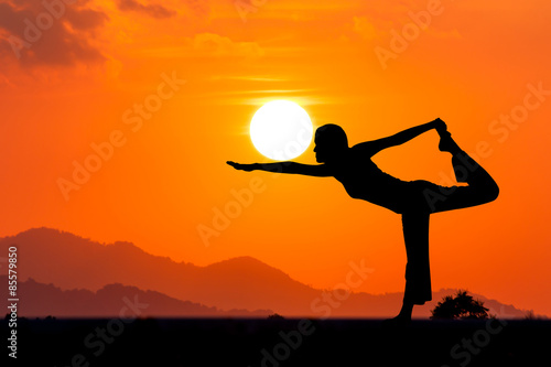 Silhouette young woman practicing yoga on the mountain at orange sunset