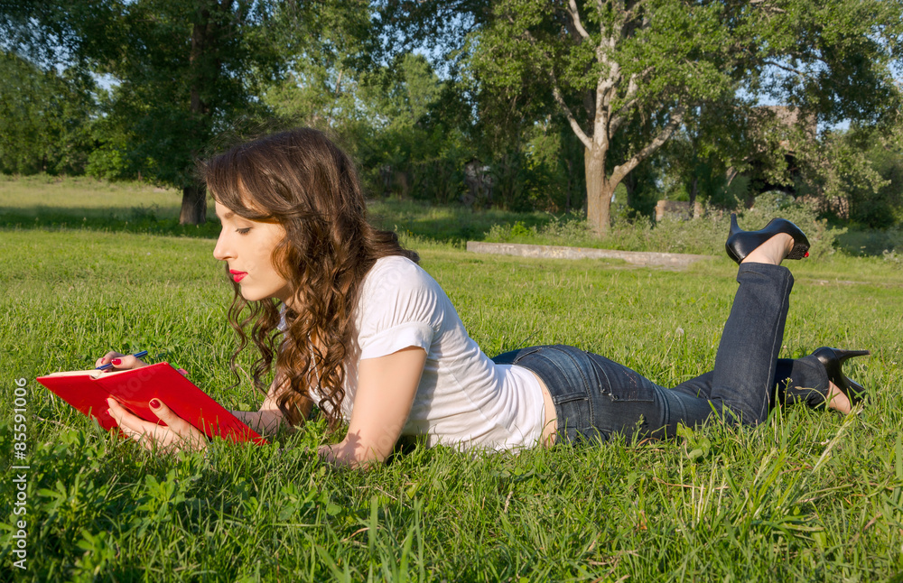 Girl with a notepad and pen in a summer park on the grass