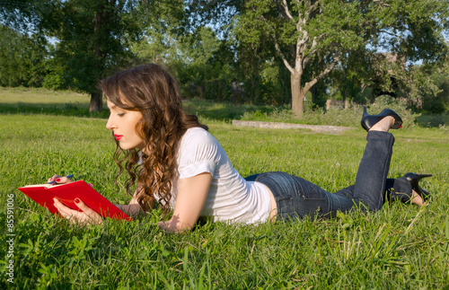 Obraz na płótnie Girl with a notepad and pen in a summer park on the grass w salonie