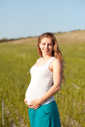 Happy pregnant woman resting in field outdoors. Smiling girl holding belly. Motherhood. Maternity.