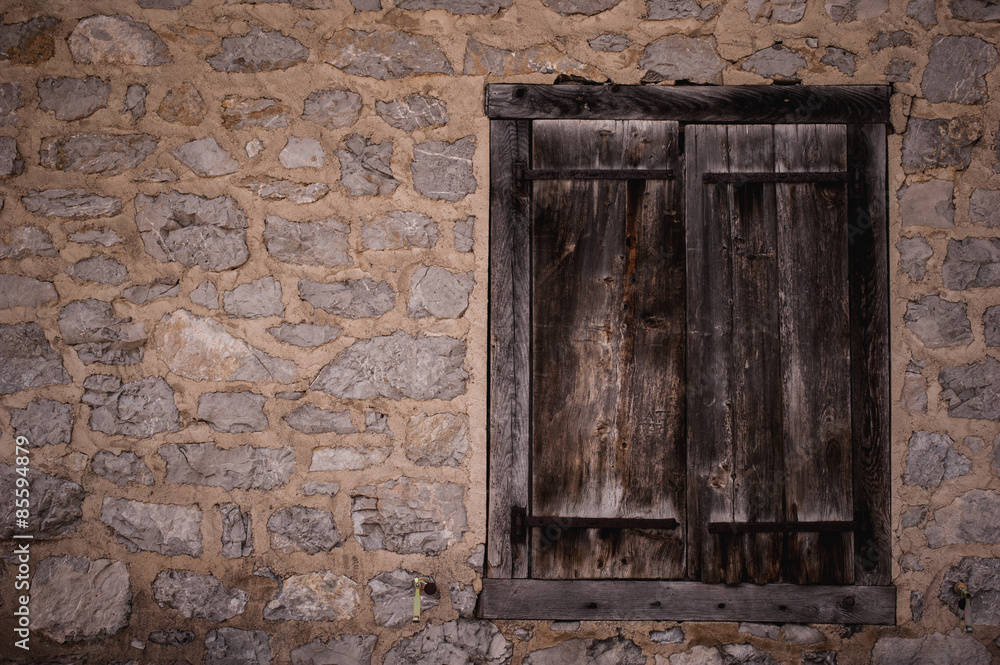 Boarded up wooden window shutter and weathered wall of derelict house.