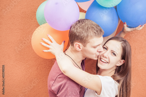 Young happy couple near the orange wall stand with balloons