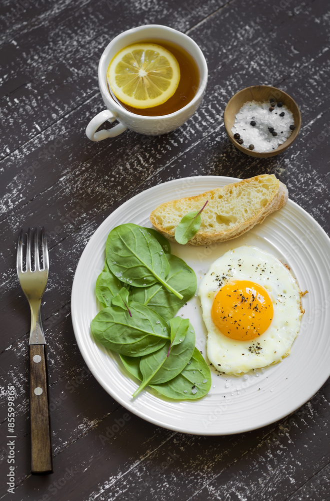 fried egg and fresh spinach on a white plate on a dark background fried egg and fresh spinach on a white plate on a dark background