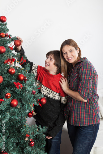 Boy and his mom smiling beside the christmas tree