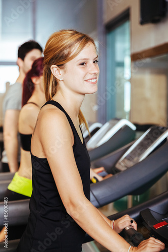 In a gym with other guys a beautiful blonde woman trains running on tapis rulant during a workout to stay in shape