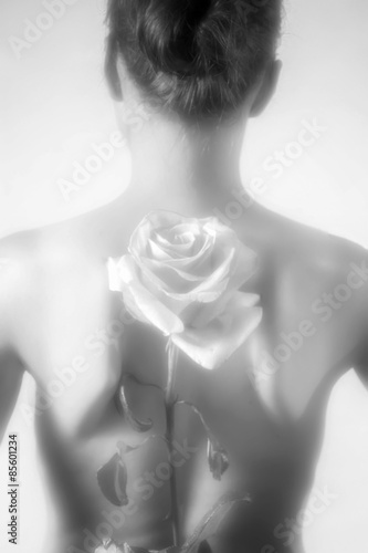 Soft image of pretty young woman holding a rose behind her back. Soft focus on flower. B W.