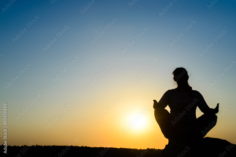 Woman meditating in front of the rising sun Woman meditating in front of the rising sun
