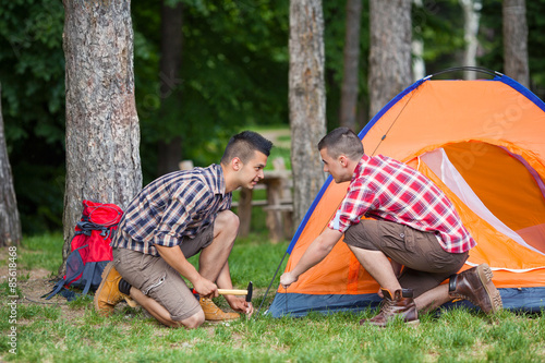 Two young men setting up a tent for camping in a forest