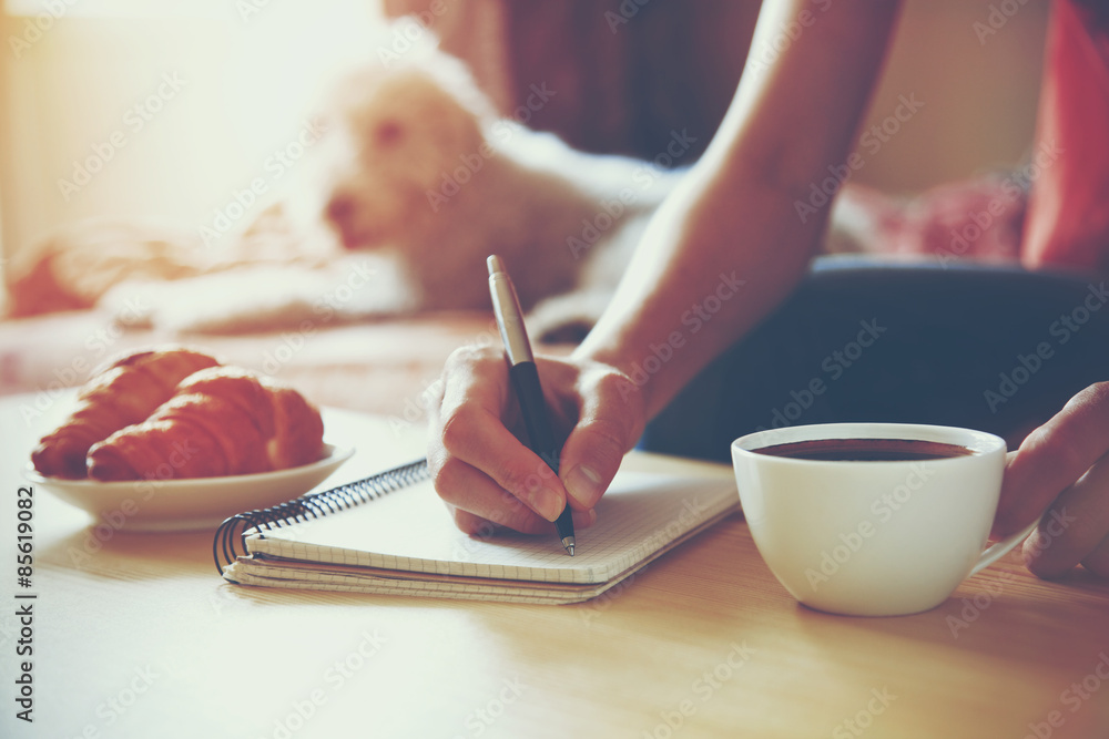Naklejka premium female hands with pen writing on notebook with morning coffee an