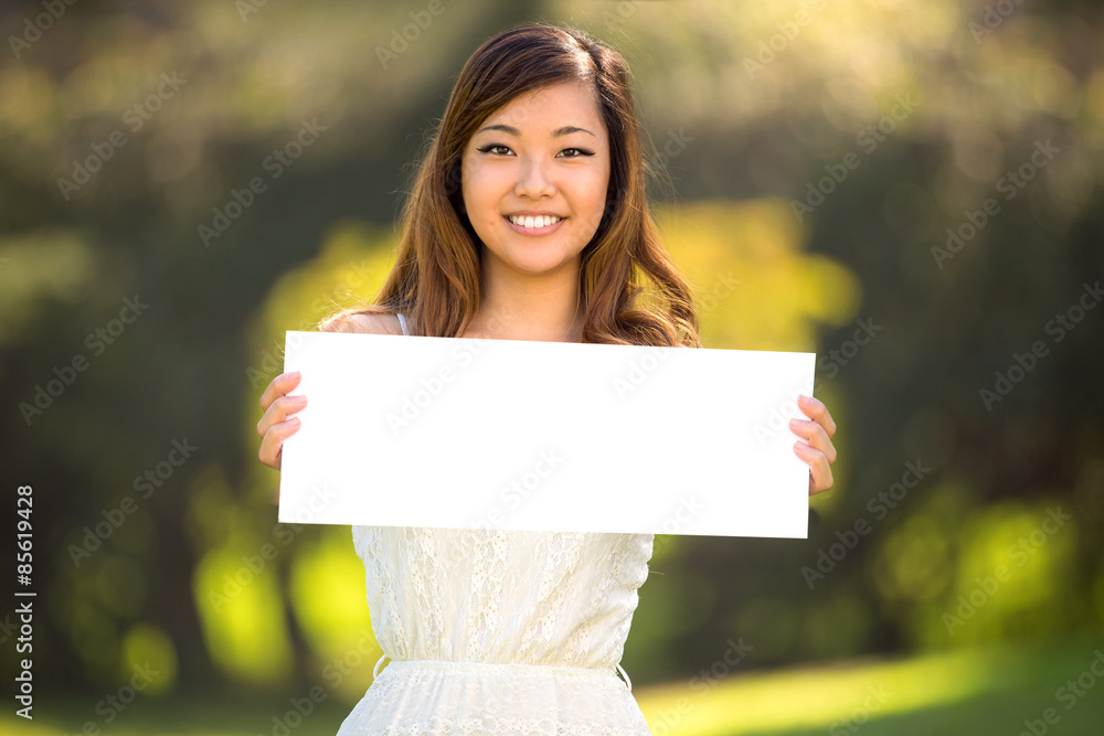 A beautiful young adult woman holding a blank white sign card outdoors smiling confident A beautiful young adult woman holding a blank white sign card outdoors smiling confident