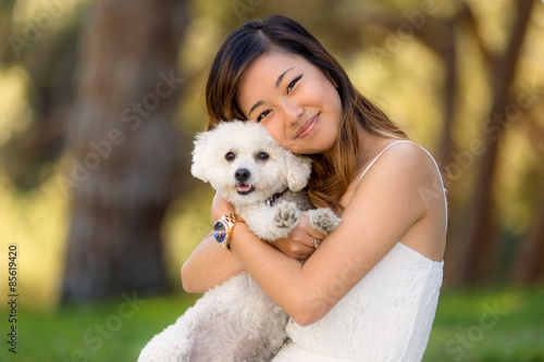 Beautiful woman with white dog smiling and hugging at the park