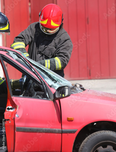 chief fireman whit red helmet while breaking the windshield