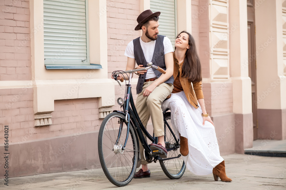 Fototapeta premium Young couple sitting on a bicycle against the wall 