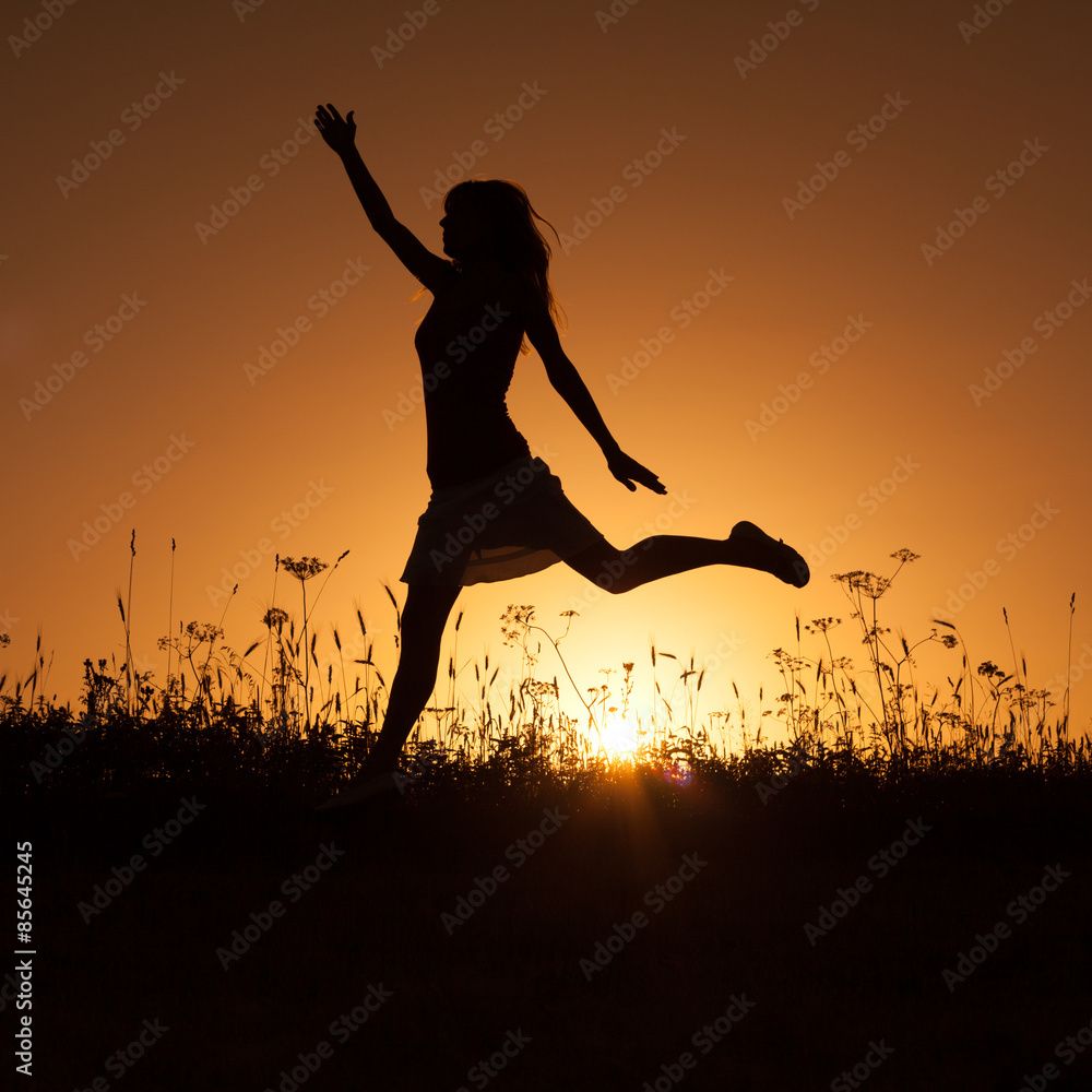 Silhouette of happy woman jumping in sunset