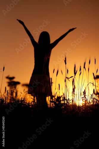 Silhouette of woman enjoying sunset, focus on wheat in foreground © djoronimo