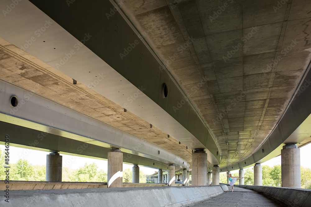 Graceful ballerina doing dance exercises on a concrete bridge 