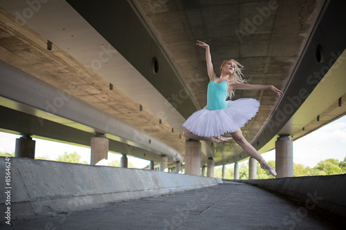 Graceful ballerina doing dance exercises on a concrete bridge 