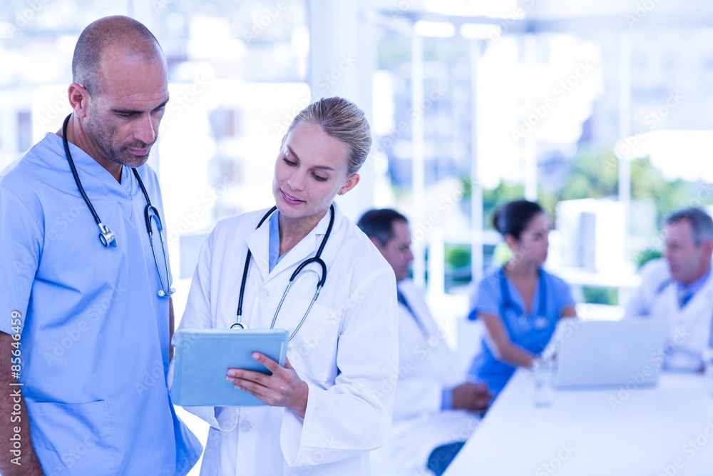 Two doctors looking at clipboard while their colleagues working Two doctors looking at clipboard while their colleagues working