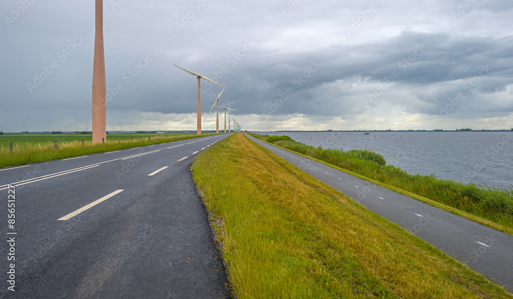 Wind farm on a dike along a lake in a cloudy summer
