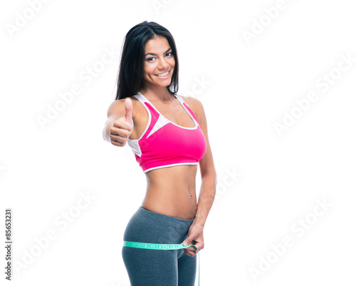 Fitness woman measure her buttocks with a measuring tape and showing thumb up isolated on a white background. Looking at camera © Drobot Dean