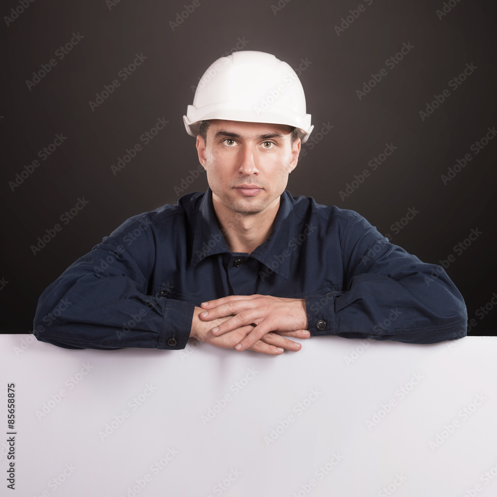 Workman in dark blue coveralls and white hardhat looking at camera Workman in dark blue coveralls and white hardhat looking at camera