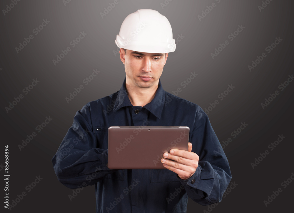 Workman in dark blue coveralls and hardhat looking at tablet pc screen Workman in dark blue coveralls and hardhat looking at tablet pc screen