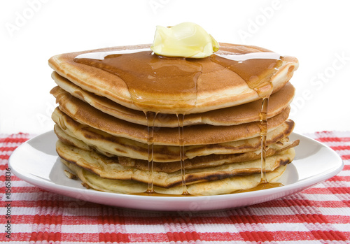 Big Stack of Pancakes – A huge stack of pancakes, covered with maple syrup and butter. On a white plate and red checked tablecloth in background.
