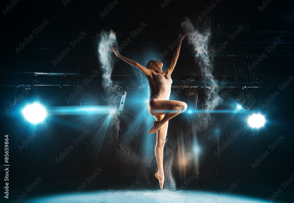 Wonderful adult ballerina posing on stage against spotlights