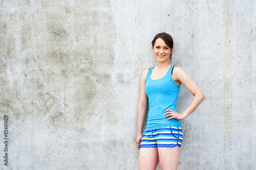 Girl in blue tank top and shorts over the wall smiling. © Wisiel