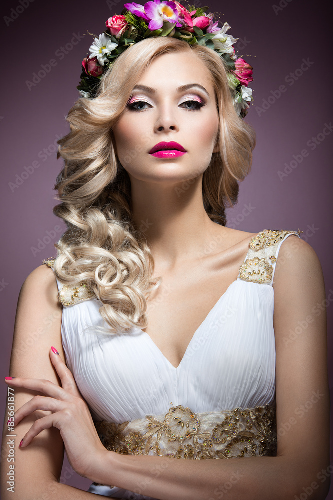 Fototapeta premium Beautiful blond girl in the image of a bride with flowers in her hair. Beauty face. Wedding image. Picture taken in the studio on a purple background.