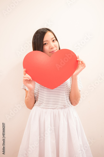 赤いハートマークを示す若い女性 © Kido
