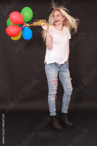 Junge blonde Frau in lässiger Pose und  modischer Jeans und Stiefel hat verschieden farbige Luftballons in der Hand . Studioaufnahme mit schwarzen Hintergrund © STphotography