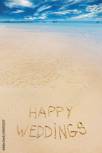 Sign of happy wedding letters written on sand at blue sky