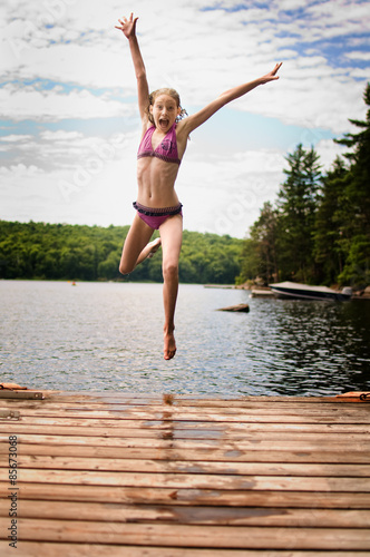 young teenage girl jumping off a dock at a lake in Ontario's cottage country