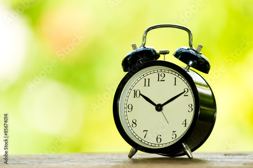 Alarm clock on table with blur green leaf background.