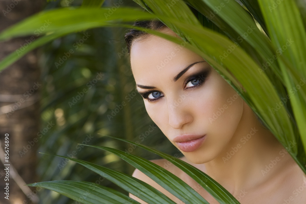 Naklejka premium Sexy beautiful woman hiding behind the palm leaves. Beautiful st