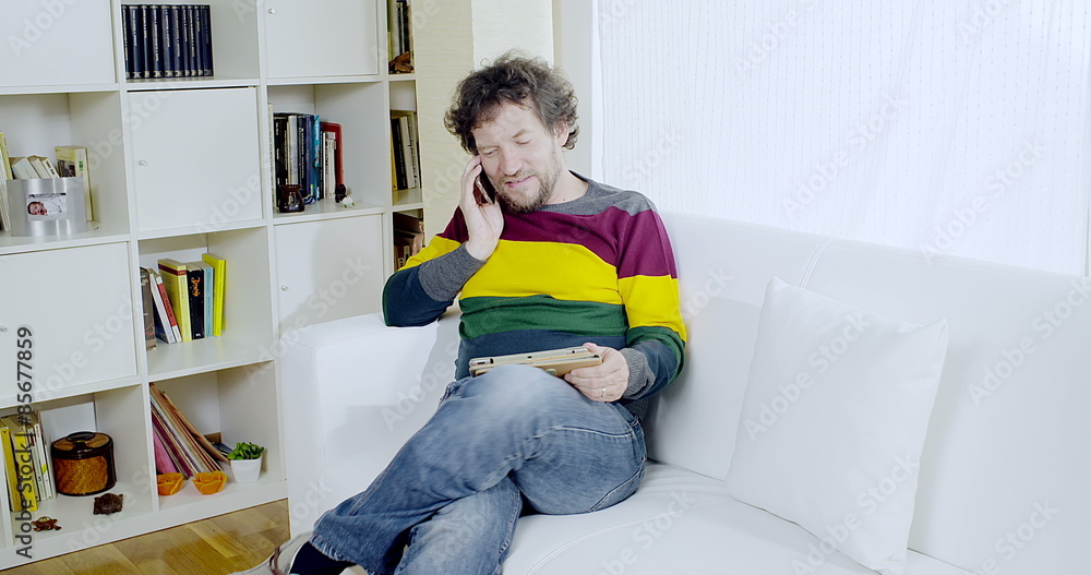 Cool man checking tablet while on the phone at home with wireless connection Cool man checking tablet while on the phone at home with wireless connection