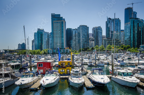 Colorful houseboats are moored in the marina in Vancouver BC alongside motor boats and sailing yachts with the city skyline in the background. © lembi