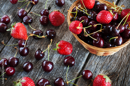 strawberries and cherries in a wicker basket on a wooden backgro